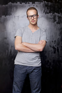 Portrait of young man with arms crossed standing against old wall