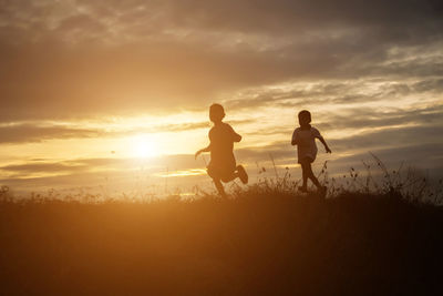 Silhouette people on field against sky during sunset