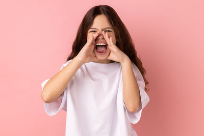 Portrait of young woman standing against pink background