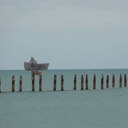 Wooden posts amidst sea against sky