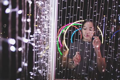 Young woman standing by illuminated string lights in room