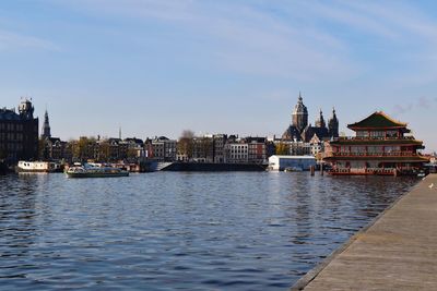 View of buildings by river against sky in city