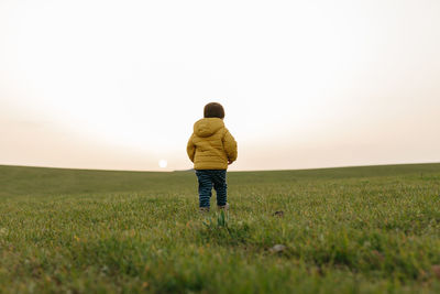 Rear view child with yellow jacket on grass