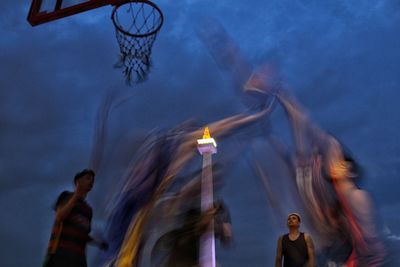 Blurred motion of people playing basketball against sky at dusk