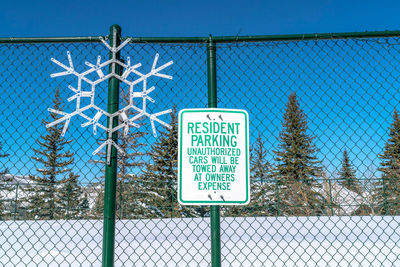 Information sign on chainlink fence against blue sky
