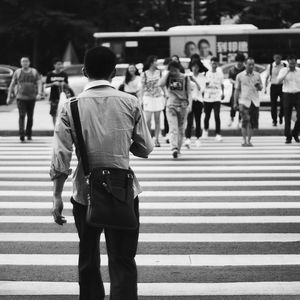 Rear view of man walking towards people crossing street