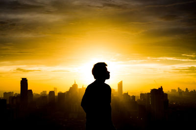 Silhouette man standing by buildings against sky during sunset