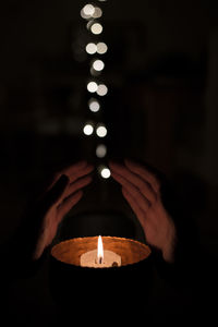 Midsection of woman gesturing by candle in darkroom