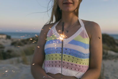 Woman holding burning sparkler at beach