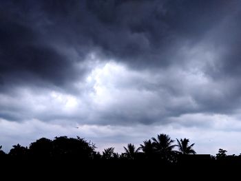 Low angle view of silhouette trees against cloudy sky