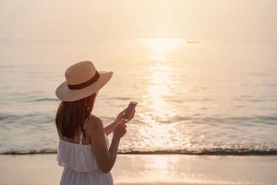 Woman standing on beach by sea against sky during sunset