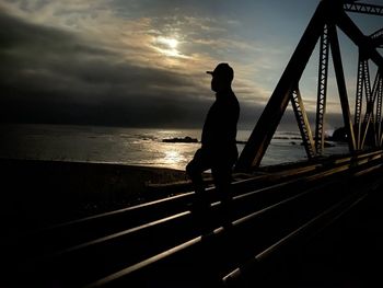 Silhouette man standing by sea against sky during sunset