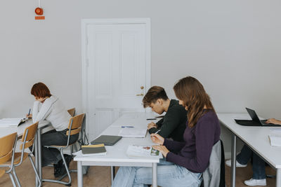 Side view of students studying at desks in classroom