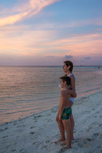 Full length of woman standing at beach against sky during sunset