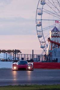 Red sports car on road against ferris wheel during sunset