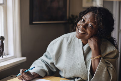 Portrait of smiling mature woman in bathrobe holding pen at home