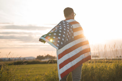 Man holding american flag while standing on field against sky