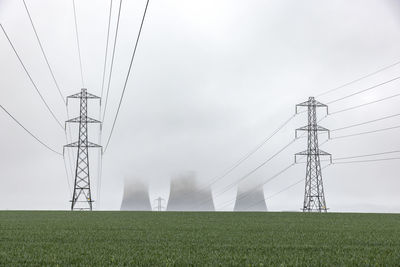 Uk, england, rugeley, electricity pylons standing in field during foggy weather with cooling towers in background