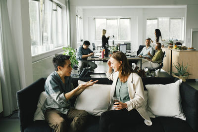 Businessman gesturing while talking to female colleague sitting on sofa at home