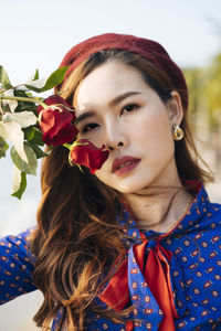 Close-up portrait of beautiful woman holding rose standing at beach