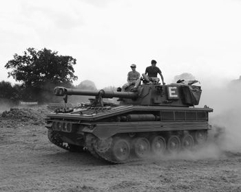 Men sitting on armored tank against sky