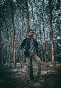 Portrait of man standing by tree trunk in forest