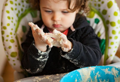 Close-up of baby girl holding dough in bowl on table at home