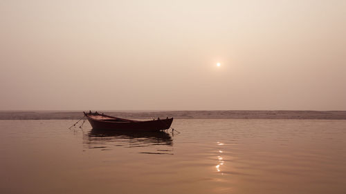 Boat moored in calm sea at sunset