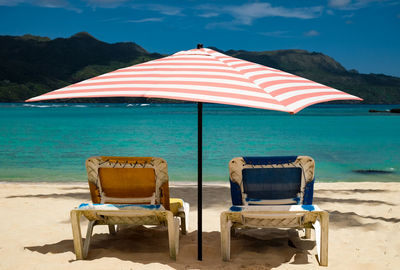 Deck chairs on beach against sky