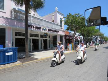 People riding motor scooters on road by shop in town