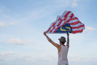 Rear view of man holding malaysian flag against sky