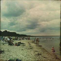 People relaxing at beach against cloudy sky