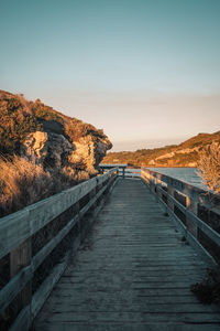 Footpath by railing against sky during sunset