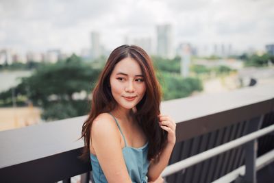 Portrait of smiling young woman standing against railing