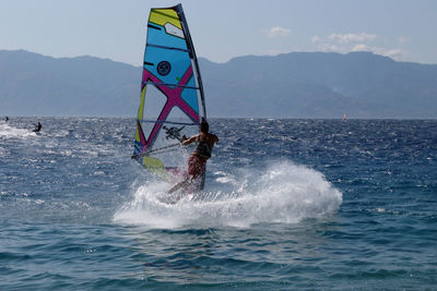 Woman windsurfing in sea against sky