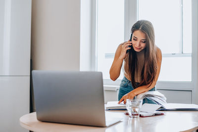 Young woman using phone while sitting on table