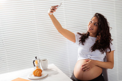 Pregnant woman taking selfie while sitting at home