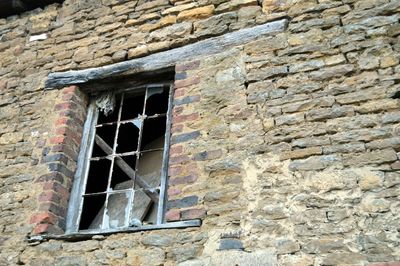 Low angle view of broken window on old building wall