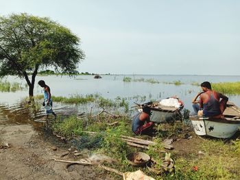 People sitting on shore by lake against sky