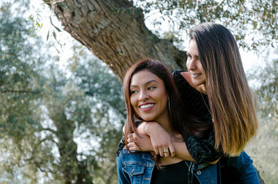 Portrait of a smiling young woman standing against tree