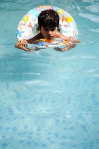 Happy indian boy swimming in a pool, kid wearing swimming costume along with air tube during day