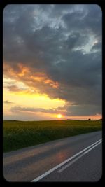 Road passing through field against cloudy sky