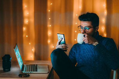 Young woman using mobile phone while sitting in illuminated room