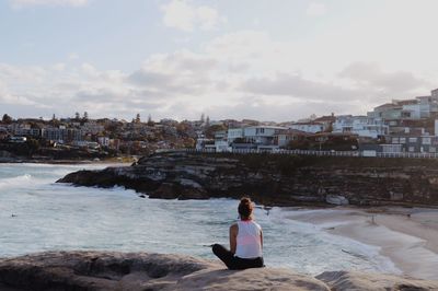 Rear view of woman sitting on sea shore against sky