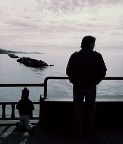 Rear view of man standing by railing against sea