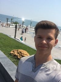 Portrait of smiling man on grass by sea against sky