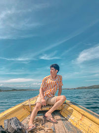 Young man sitting on boat in sea against sky