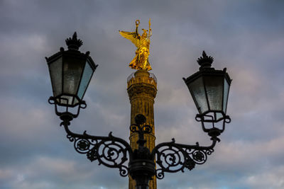 Low angle view of victory column and street light against cloudy sky