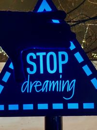 Low angle view of illuminated text on blue sign