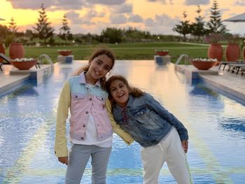 Portrait of smiling two young girls  standing against sky near a pool
